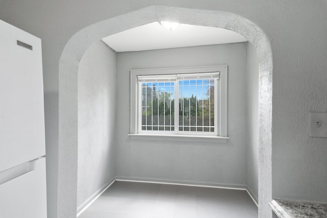 spare room with arched walkways, baseboards, and tile patterned floors