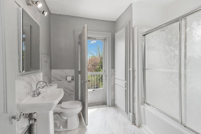 full bathroom with bath / shower combo with glass door, toilet, marble finish floor, and wainscoting