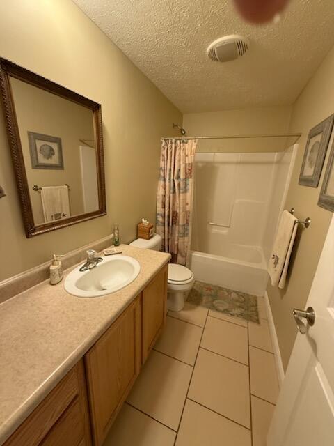 full bath featuring vanity, shower / bath combination with curtain, toilet, a textured ceiling, and tile patterned floors