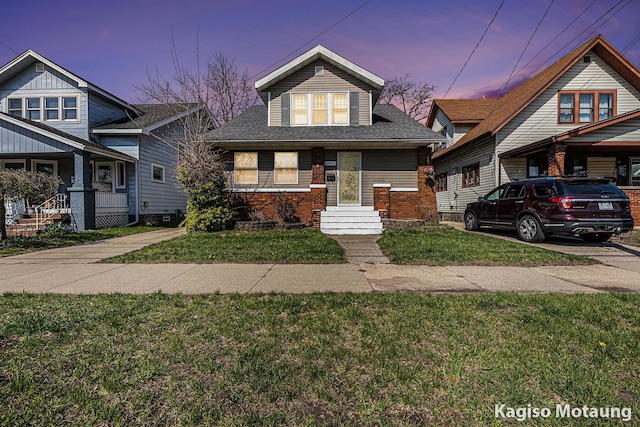 bungalow with a lawn, brick siding, and roof with shingles