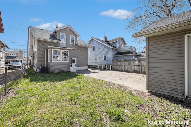 rear view of house featuring a yard, fence, driveway, and roof with shingles