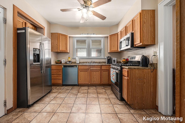 kitchen with a ceiling fan, dark countertops, brown cabinets, a sink, and stainless steel appliances