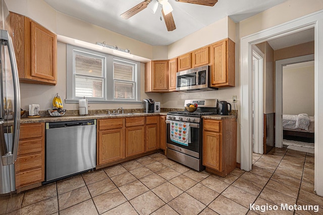 kitchen featuring dark countertops, ceiling fan, a sink, appliances with stainless steel finishes, and light tile patterned floors