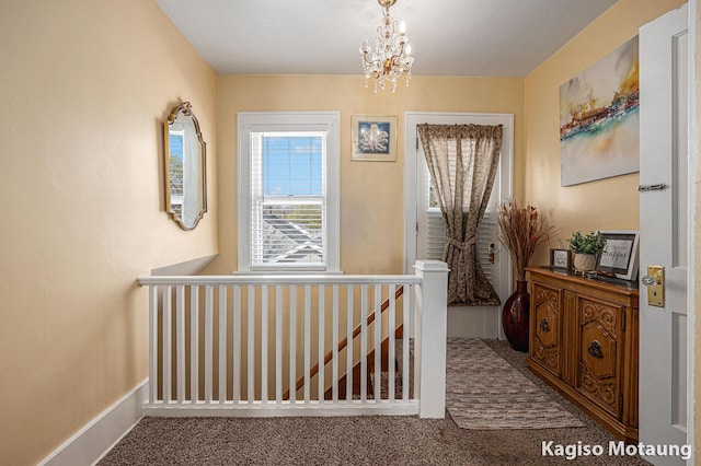 corridor with carpet flooring, a chandelier, and an upstairs landing