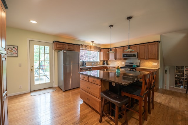 kitchen featuring appliances with stainless steel finishes, a center island, a kitchen breakfast bar, backsplash, and light wood-type flooring