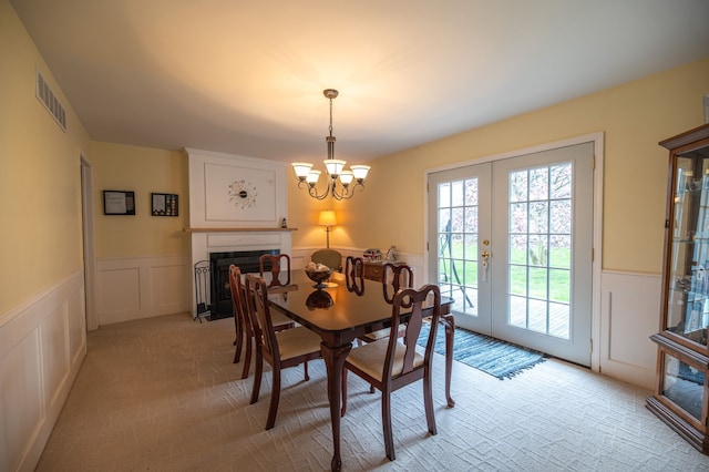 dining space featuring a decorative wall, a wainscoted wall, french doors, visible vents, and a fireplace with flush hearth