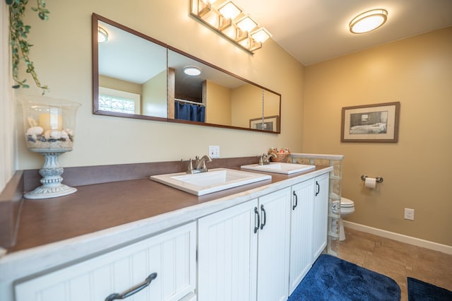bathroom with double vanity, toilet, baseboards, and a sink