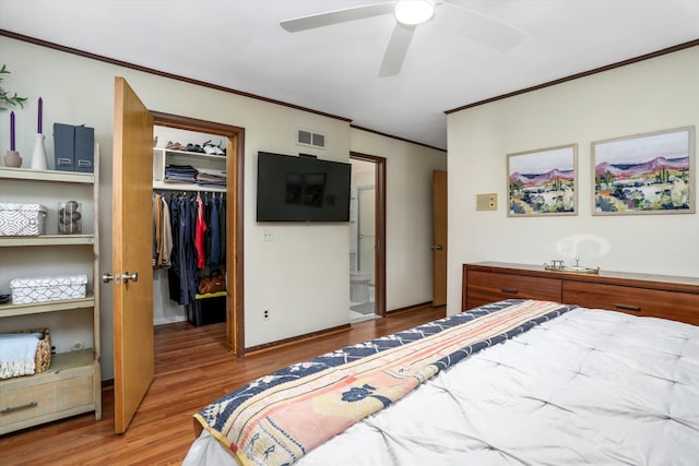 bedroom with a walk in closet, wood finished floors, visible vents, ornamental molding, and a closet