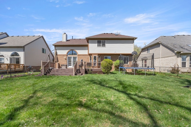 back of property featuring a lawn, brick siding, a trampoline, and a deck