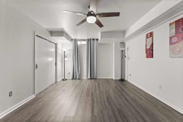 interior space with baseboards, ceiling fan, and dark wood-type flooring