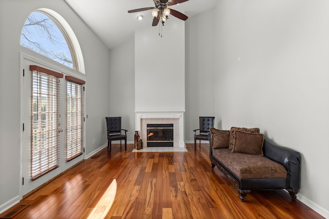 living area featuring wood finished floors, high vaulted ceiling, ceiling fan, and a fireplace