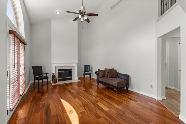 sitting room featuring visible vents, a towering ceiling, wood finished floors, ceiling fan, and a tiled fireplace