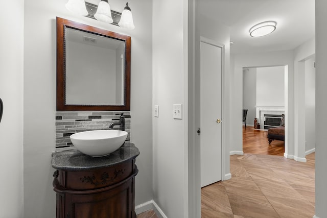 bathroom with backsplash, baseboards, a glass covered fireplace, and vanity