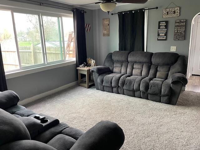 carpeted living room featuring baseboards, a ceiling fan, and arched walkways