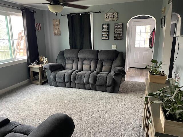 living area featuring baseboards, arched walkways, ceiling fan, and a healthy amount of sunlight