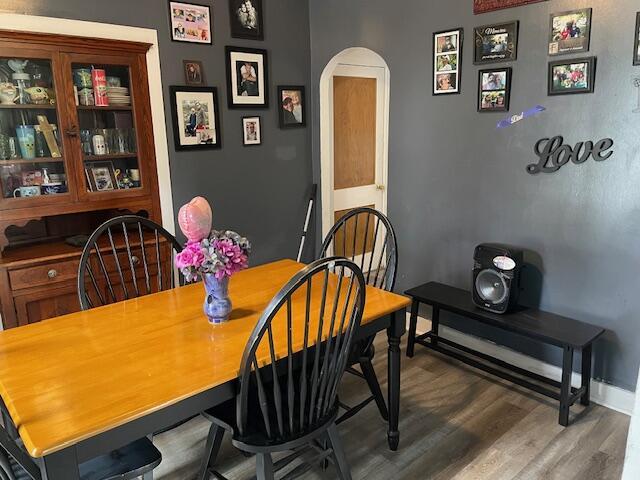 dining space featuring arched walkways, baseboards, and wood finished floors