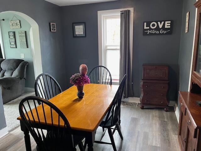 dining area featuring arched walkways, baseboards, and light wood-type flooring
