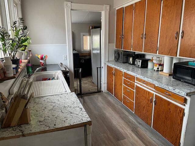 kitchen with brown cabinetry, black microwave, dark wood finished floors, light countertops, and freestanding refrigerator