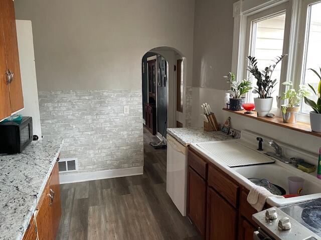 kitchen with brown cabinets, black microwave, arched walkways, dark wood finished floors, and baseboards