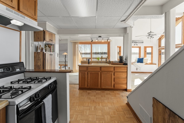 kitchen with brown cabinets, a sink, gas stove, under cabinet range hood, and visible vents
