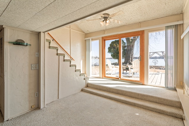 unfurnished living room featuring a ceiling fan, carpet, a textured wall, and stairway