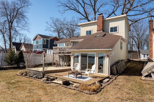 back of house featuring a chimney, a wooden deck, fence, a yard, and a shingled roof