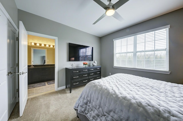 bedroom featuring baseboards, ensuite bathroom, light carpet, and ceiling fan