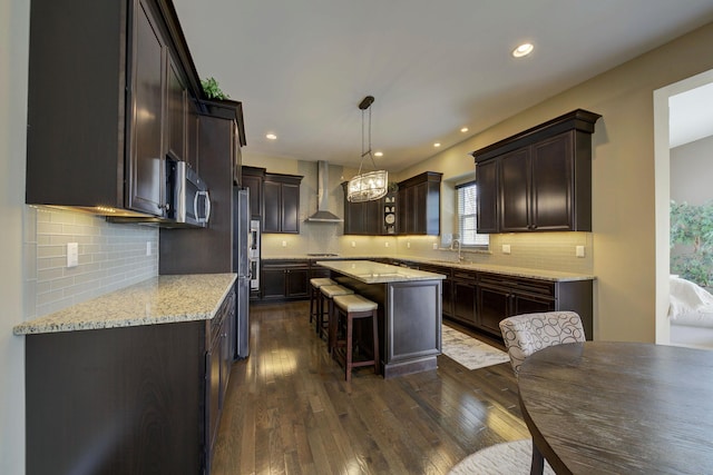 kitchen featuring wall chimney range hood, tasteful backsplash, dark brown cabinetry, and a kitchen bar