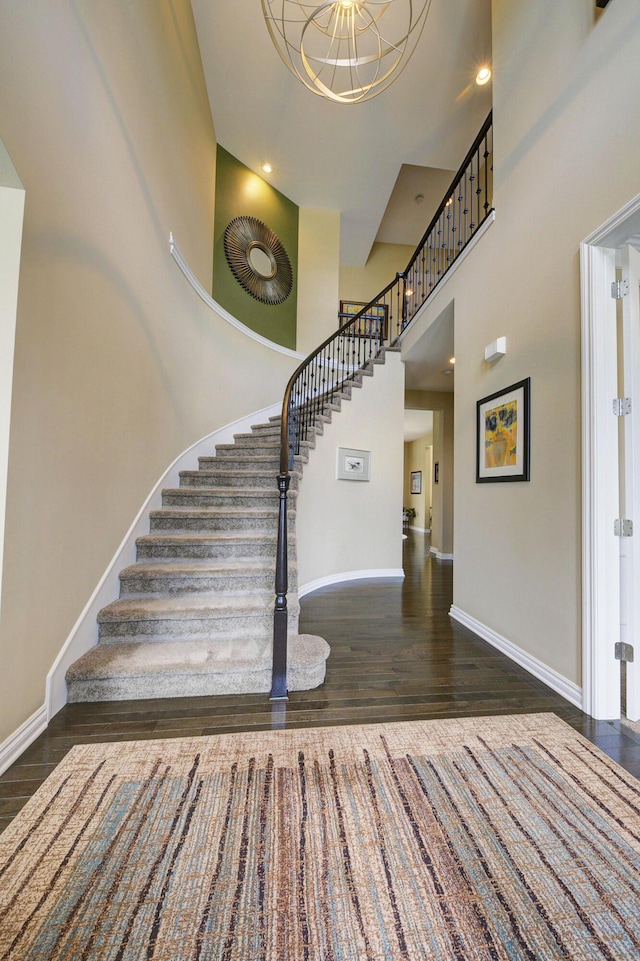 stairs with baseboards, a high ceiling, wood finished floors, and a notable chandelier