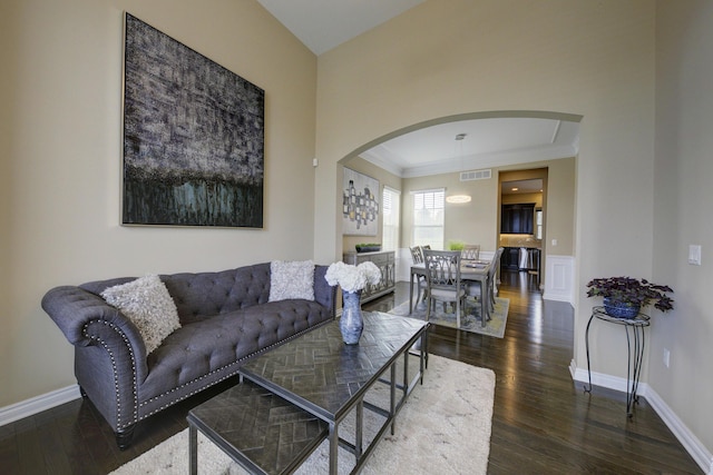 living room with crown molding, visible vents, hardwood / wood-style floors, baseboards, and arched walkways