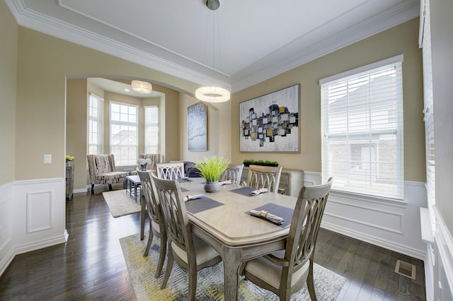 dining area featuring crown molding, a wainscoted wall, arched walkways, and dark wood-type flooring