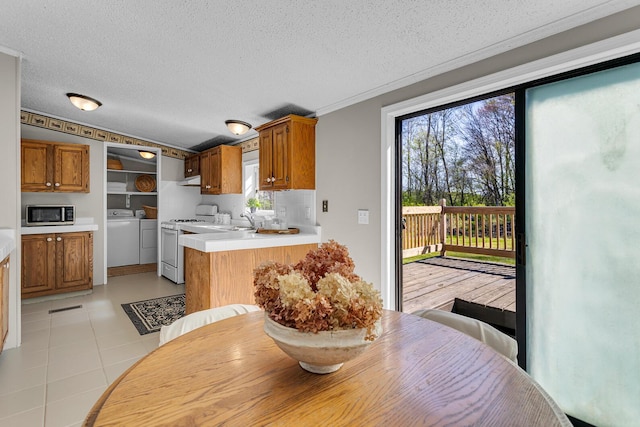 kitchen with white gas stove, stainless steel microwave, brown cabinetry, and washer and clothes dryer
