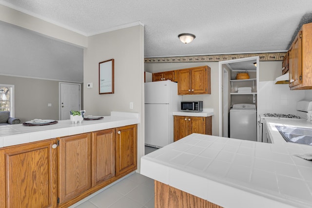 kitchen with a peninsula, tile countertops, white appliances, and washer / clothes dryer