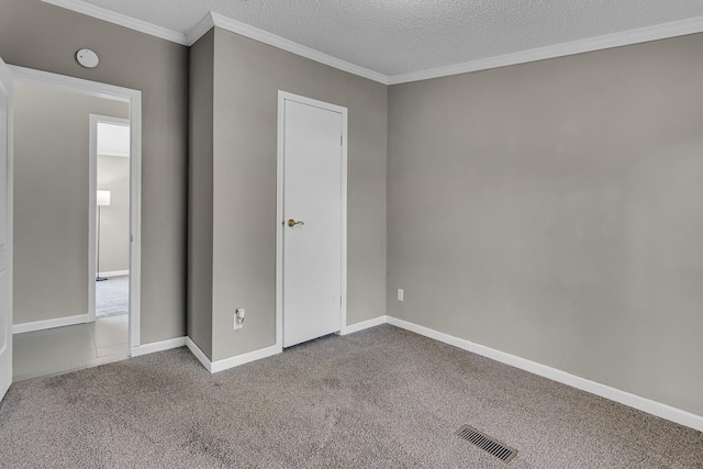 unfurnished bedroom featuring carpet floors, a textured ceiling, baseboards, visible vents, and ornamental molding