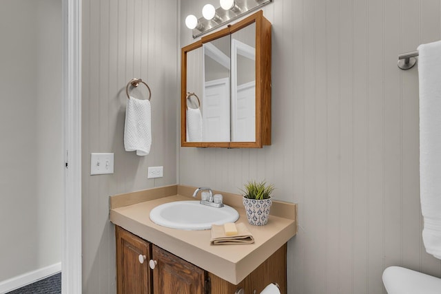 bathroom featuring toilet, wood walls, and vanity