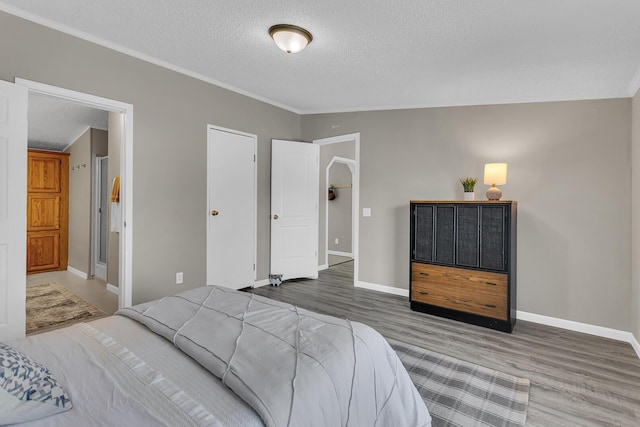 bedroom featuring crown molding, a textured ceiling, baseboards, and wood finished floors