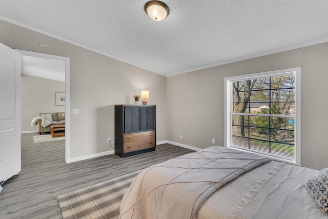 bedroom with baseboards, ornamental molding, a textured ceiling, and wood finished floors