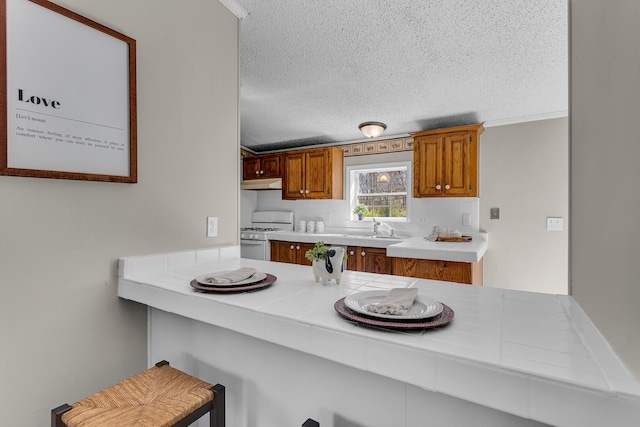 kitchen featuring gas range gas stove, tile counters, a textured ceiling, under cabinet range hood, and a sink