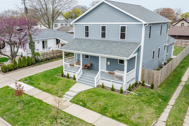 view of front facade with fence, covered porch, a shingled roof, and a front lawn