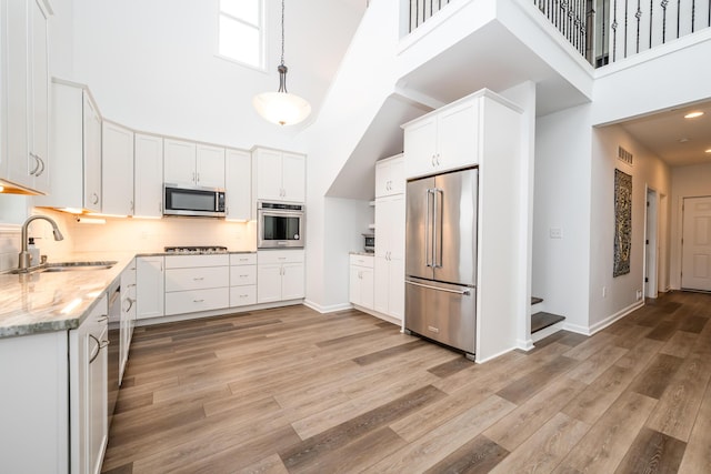 kitchen featuring a high ceiling, appliances with stainless steel finishes, a sink, and light stone countertops