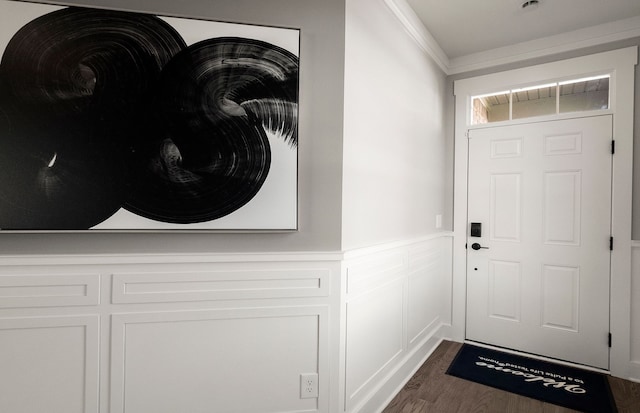 doorway to outside featuring crown molding, a decorative wall, dark wood finished floors, and a wainscoted wall
