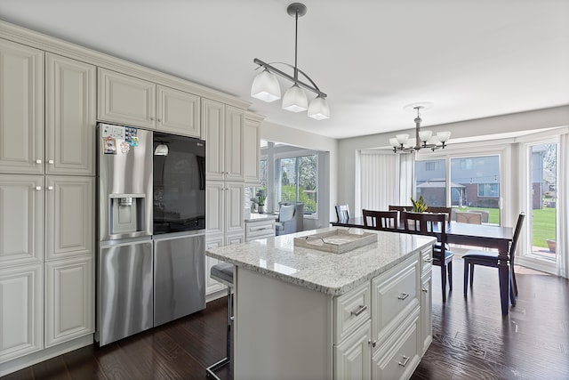 kitchen featuring light stone countertops, dark wood-style floors, a center island, a chandelier, and stainless steel fridge with ice dispenser