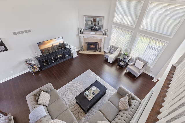 living room with visible vents, a towering ceiling, a fireplace, wood finished floors, and baseboards