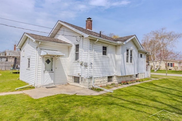 rear view of property featuring a yard, a chimney, and a trampoline