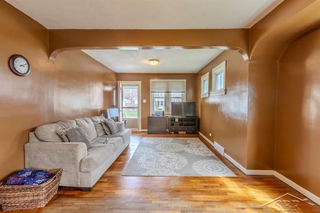 living area with arched walkways, baseboards, visible vents, and wood finished floors