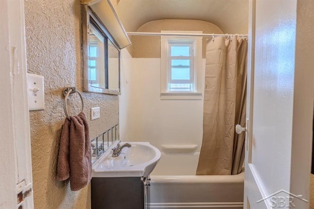 full bath with vanity, a textured wall, vaulted ceiling, and shower / tub combo