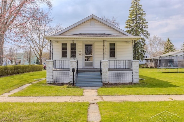 bungalow-style home featuring a trampoline, a front lawn, and covered porch