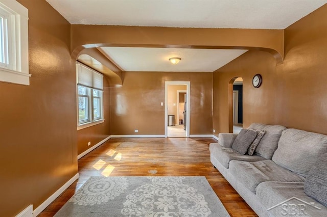 living area with arched walkways, baseboards, visible vents, and wood finished floors