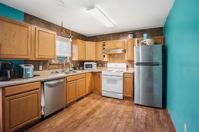 kitchen with light countertops, under cabinet range hood, a sink, light wood-style flooring, and appliances with stainless steel finishes