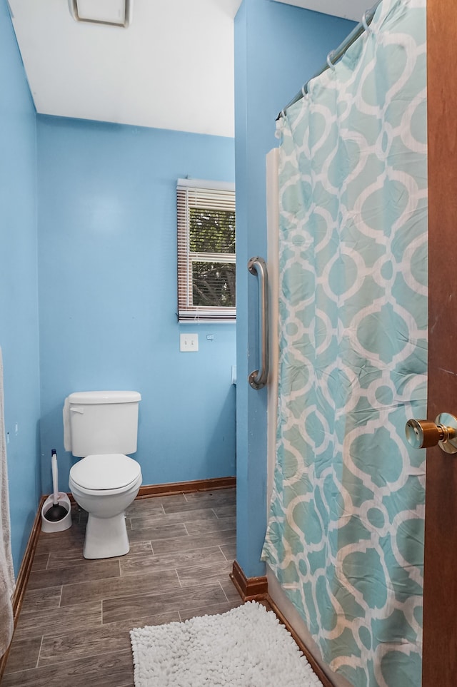 bathroom with baseboards, curtained shower, wood finish floors, and toilet